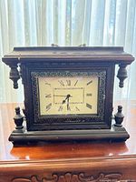 Front view of dark brown wood mantel clock showing dial, turned columns, moulded frame