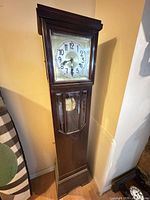 Full front view of grandfather clock showing entire wood case and pendulum window