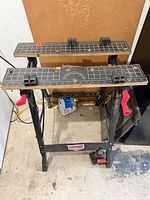 Overall view of Jobmate folding portable workbench showing grid-printed wood surfaces, clamp handles and metal frame