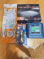 All four packaged items: truck bed LED strip set, puck light kit, crank flashlight, Magellan RoadMate 1340 GPS