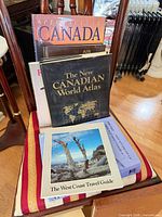 Stack of books on chair showing Spectacular Canada, Air, New Canadian World Atlas, West Coast Travel Guide and others