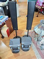 Front view of two tall Sony satellite speakers on stands and two bass speaker cabinets