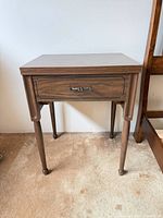 Front view of closed sewing machine cabinet showing walnut finish, tapered legs, and drawer front