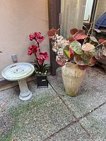 Group shot showing birdbath, black planter with red flowers, beige floor vase with foliage