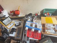 Assortment on table: drill bit sets, fluorescent tubes, wooden hardware box, fuel can, rod holder