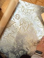Silver metallic floral wallpaper partially unrolled
