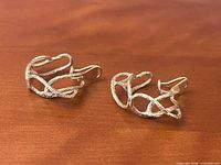 Two textured 14K gold clip-on earrings on wood surface, openwork design visible