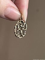 Front view of pendant held between fingers showing openwork design and bail