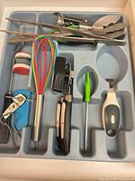 Grey organiser with whisk, can openers, peeler, skewers, pasta server, meat fork