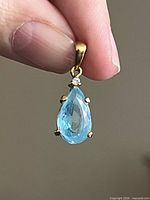 Front view of pendant showing blue pear stone, clear accent, and yellow metal bail