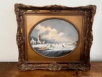Full view of framed oval oil painting depicting winter village scene