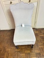Front view of light grey upholstered slipper chair showing scalloped back and dark wood legs