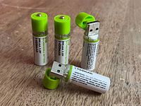 Four USB-rechargeable AA batteries standing with caps on and off showing USB plugs