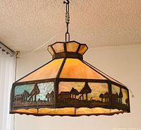 Full view of hanging slag glass lamp lit, showing glass colors and metal overlay scene
