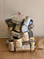 Front view of clear bag filled with empty silver and gold tone tin cans