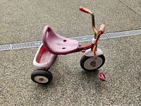 Side view of red Radio Flyer tricycle on concrete surface