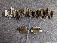 Row of thirteen cabinet door hinges displayed on fabric surface