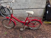 Full left side view of red children’s bike showing frame, wheels, handlebars and seat