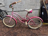 Right side profile of pink girls cruiser bike leaning against wall