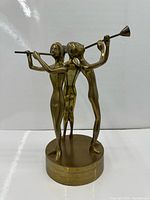 Front view of brass sculpture showing three musicians and circular base