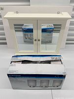 Front view of medicine cabinet with mirrored doors and boxed Westinghouse vanity light