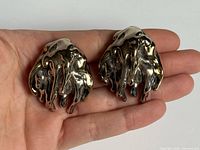 Pair of sterling silver abstract clip-on earrings shown in hand to indicate size and design detail