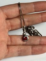 Pendant on hand showing red garnet bezel set in sterling silver with accent stone and box chain