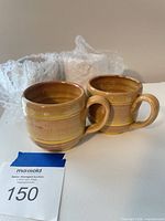 Two tan glazed stoneware mugs with lot tag