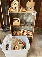 Shelf with two medium birdhouses, triangular wood parts, various small craft items and storage tub below