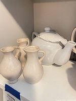 White ceramic teapot with three cream mini pitchers on shelf
