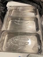 Three stainless steel food pans with clear lids in packaging