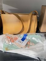 Front view of mustard yellow Lamarthe shoulder bag, gloves in clear packaging, white dust bag