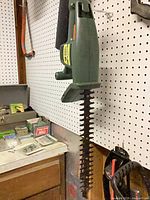 Green electric hedge trimmer hanging on pegboard