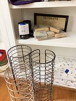 Overall lot showing three wire holders, bag of soaps and framed sign on shelf