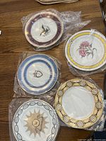 Five stacks of assorted small porcelain plates in plastic wrap