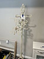 Full view of cream metal coat rack with scrollwork arms and tripod base