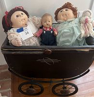 Three dolls seated inside black vintage doll carriage