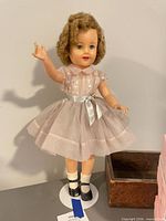 Full view Shirley Temple doll on stand, dress and shoes visible