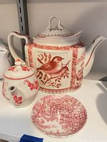 Front view of teapot with lid, bird motif visible, plate and teapot base shown