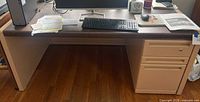 Front view of rectangular desk showing dark brown top, beige/cream sides and pedestal