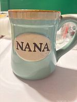 Front view showing teal mug with cream oval plaque embossed NANA