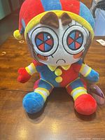 Front view of Pomni plush showing colors, facial embroidery, tags attached
