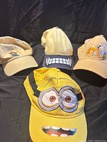 Four cartoon character baseball caps displayed on black cloth
