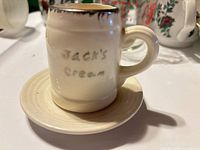 Front view of creamer on saucer showing hand lettering and drip glaze