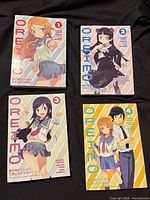 Front covers of Oreimo volumes 1-4 arrayed on black cloth