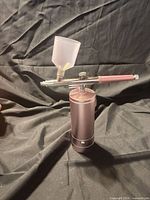 Full view of cordless airbrush standing upright showing compressor base, airbrush body, and paint cup