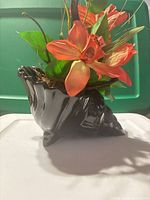 Side view of black glazed conch shell vase with flowers