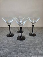 Front view of four martini glasses showing clear bowls and black stems