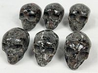 Six grey crystal skull carvings grouped on white surface