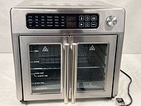 Front view of the stainless steel Emeril Lagasse French Door AirFryer 360 showing double glass doors, control panel and power cord